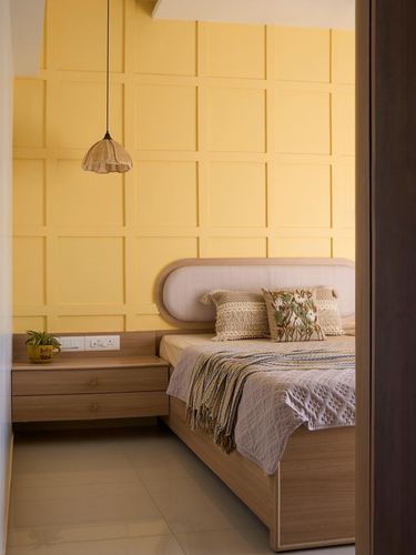 Bedroom corner with mustard grid-panel wall, curved beige headboard, wicker pendant light, and wooden floating nightstand.