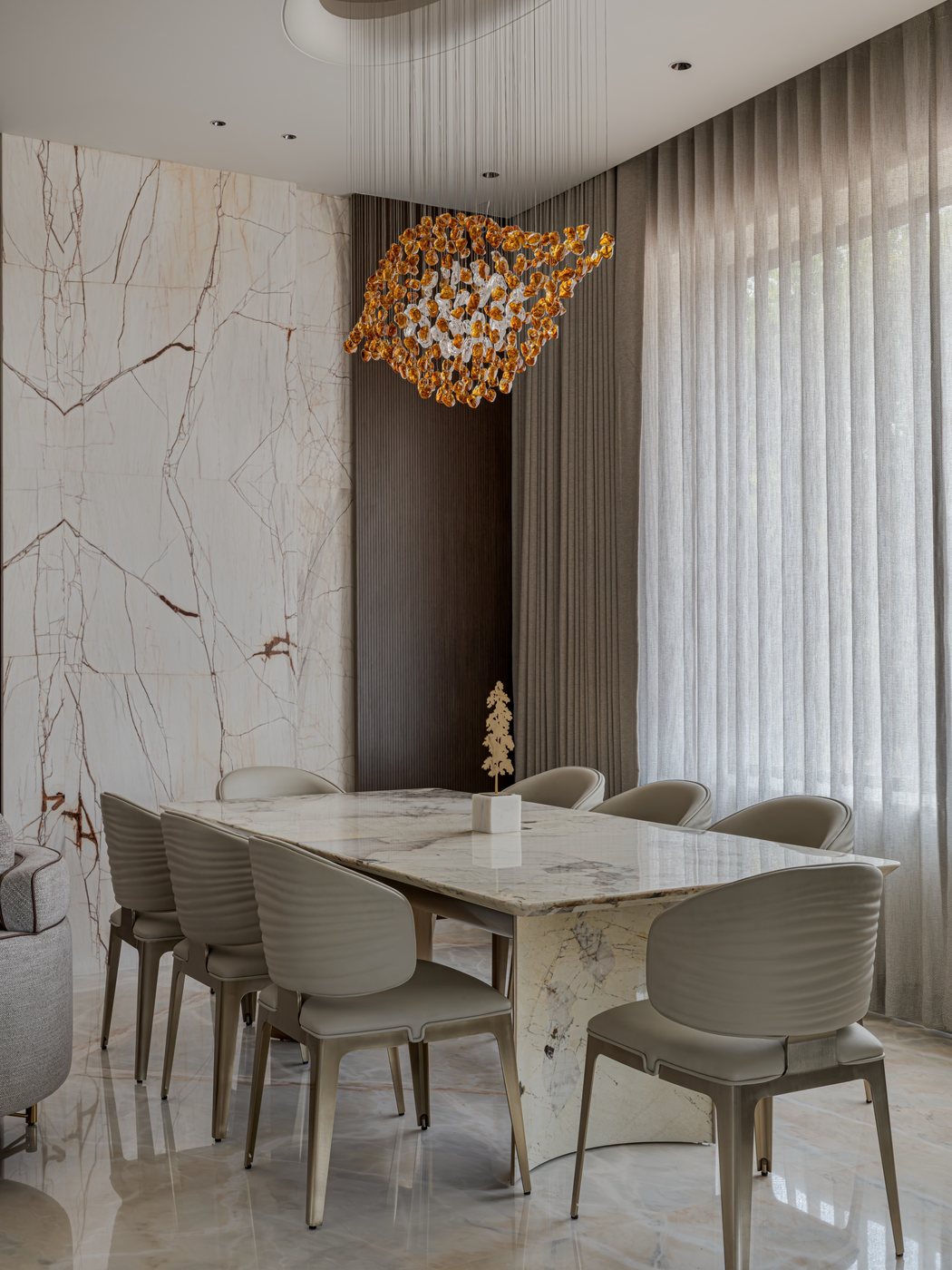 Dining room with marble-top table, ribbed chairs, and an amber floral pendant light against a marble feature wall.