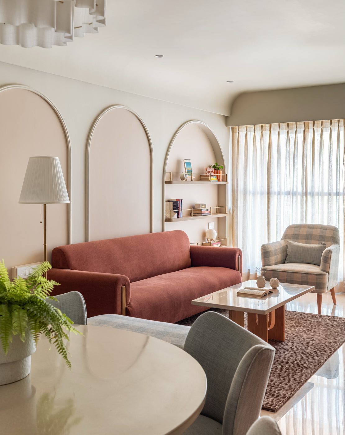 Living room with terracotta sofa, arched wall paneling, checkered armchair, and marble coffee table in soft daylight