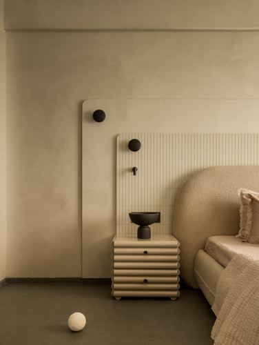 Beige bedroom corner with ribbed nightstand, round black sconces, and bouclé headboard