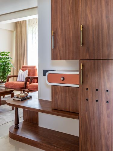 Wooden foyer cabinetry with brass handles beside a curved console table and orange armchair in living area.