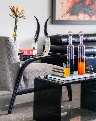 Coffee table vignette with colored glass decanters, marble tray, and horn sculptures beside a leather sofa