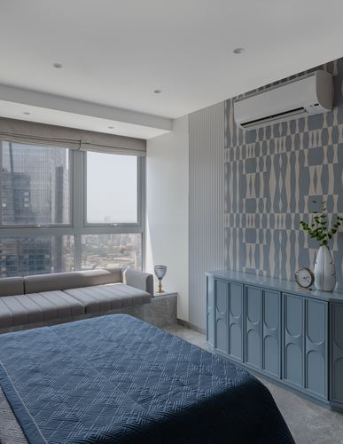 Bedroom with blue geometric wallpaper, blue cabinet, window seat, and city skyline view