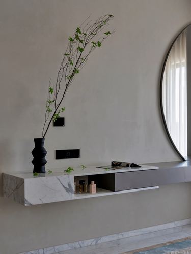 Floating marble console with black vase and branch under a round mirror on a plastered wall