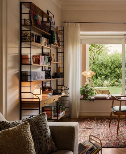 Living room corner with black ladder bookshelf, window seat, and patterned rug in warm light