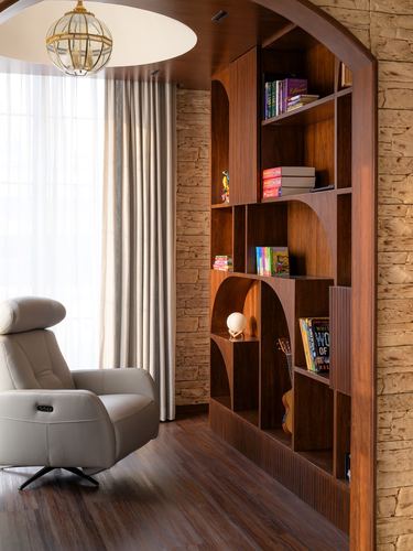 Arched wooden bookshelf niche beside a grey recliner and sheer-curtained window