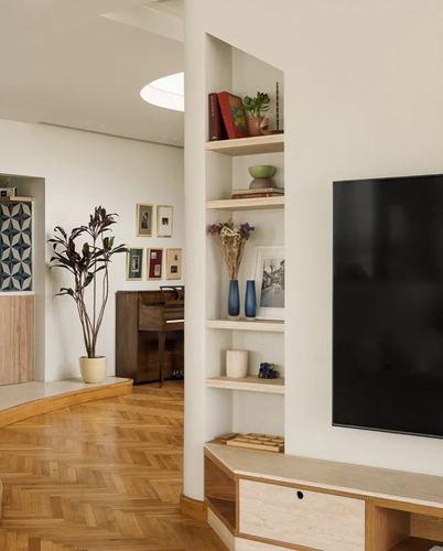 Curved plaster niche with wooden shelves, TV, and view into living room with piano and herringbone floor