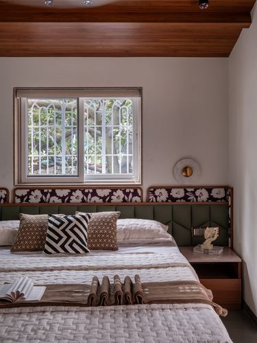 Bedroom with patterned upholstered headboard, wood ceiling, window with decorative grille and greenery view