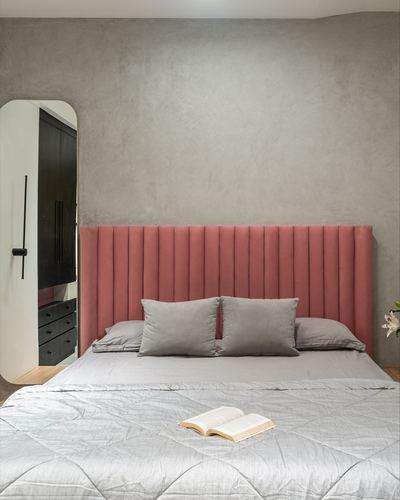 Bedroom with dusty rose fluted velvet headboard, grey plaster wall, and arched mirror beside dark wardrobe