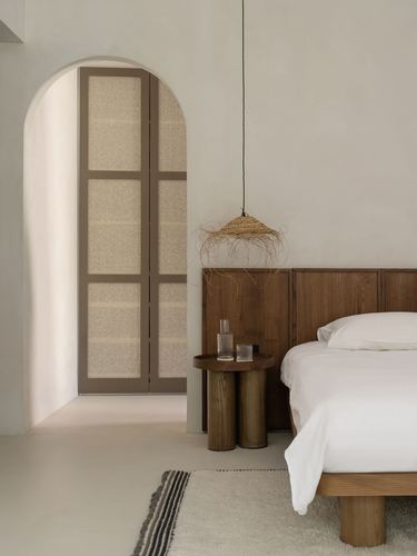 Bedroom with arched doorway, wood headboard, cane pendant light, plaster walls