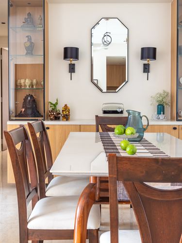 Dining table with wooden chairs facing a marble-topped sideboard and octagonal mirror flanked by sconces