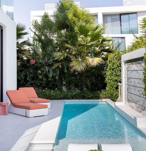 Villa courtyard with turquoise pool, terracotta loungers, palm trees and white stone facade in Dubai