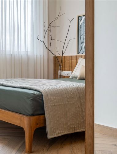 Bedroom corner with sage green bedding, fluted wooden headboard, sheer curtains and a dried branch decoration