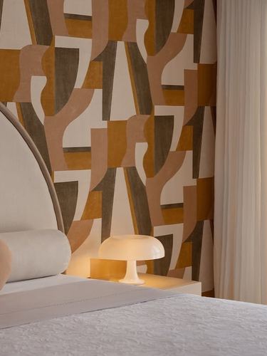 Bedroom corner with arched upholstered headboard, mushroom lamp, and bold geometric mustard wallpaper