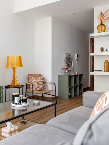 Living room corner with amber lamp, rattan chair, green shelving unit and wood flooring