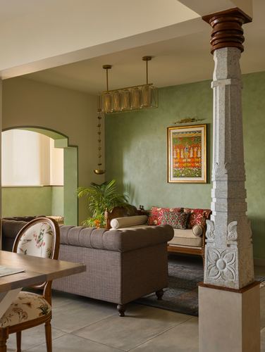 Living room with carved stone column, green walls, tufted ottoman and framed traditional art