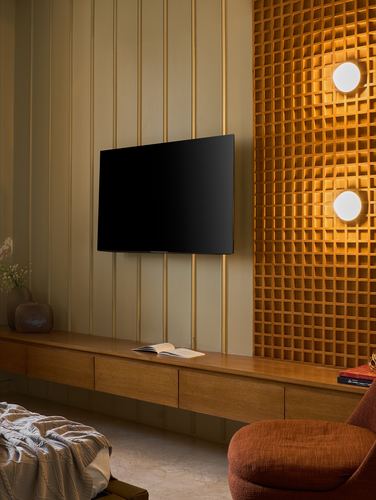 Living room with wood-panelled wall, wall-mounted tv, floating console, and glowing textured amber wall behind sphere lights
