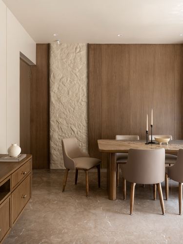 Dining area with fluted wood wall, textured stone niche, marble table and taupe chairs