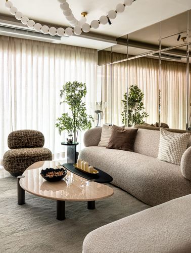 Beige living room with boucle sofa, round marble coffee table, and mirrored wall reflecting sheer curtains