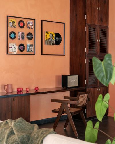 Terracotta wall with framed vinyl records above a wooden console and cane chair