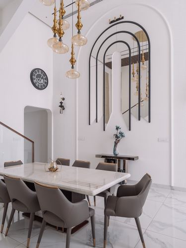 Marble dining table with taupe leather chairs beneath brass pendant lights and arched mirror art on curved white wall