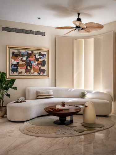Curved cream sofa with round wood table and layered rugs beneath a palm-leaf ceiling fan
