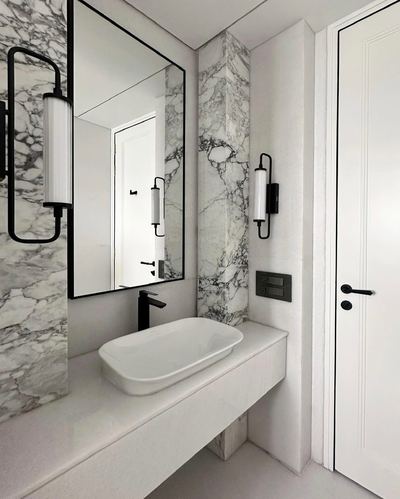 White marble bathroom with black-framed mirror, vessel sink, and matte black wall sconces beside a panelled door