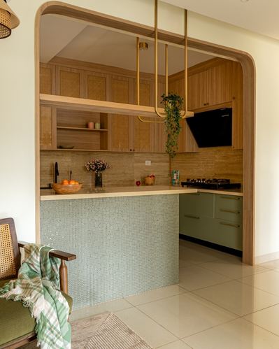 Arched wooden doorway framing a kitchen with sage green island and brass pendant lights, Bangalore apartment