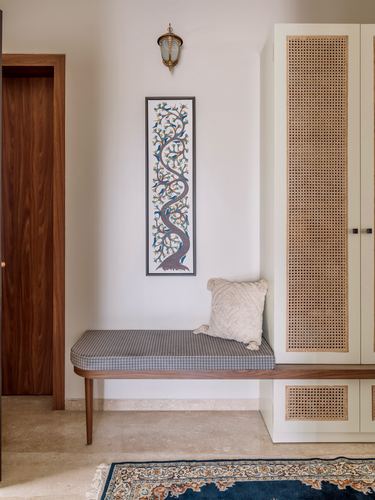 Foyer bench beneath framed tree artwork next to cane-fronted wardrobe