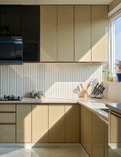 L-shaped kitchen with beige glossy cabinets, fluted white backsplash, and strong diagonal sunlight