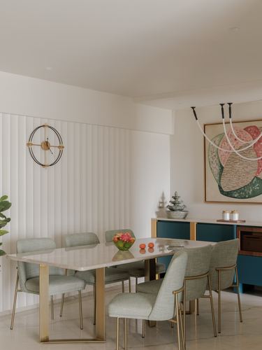 Dining room with marble table, sage green chairs, brass legs, fluted wall and teal credenza