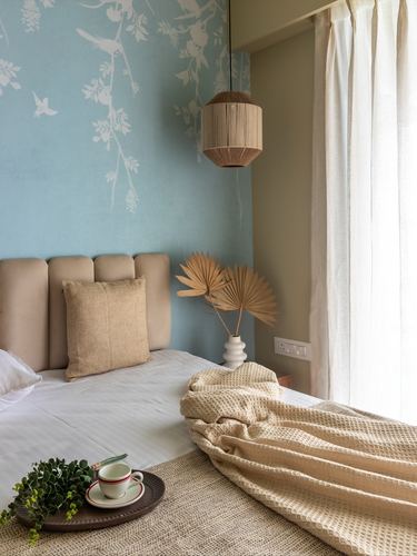 Bedroom corner with pale blue bird mural wallpaper, cane pendant light and beige upholstered headboard
