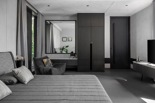 Grey monochrome bedroom with dark wardrobe wall, mirror, armchair, and layered bedding
