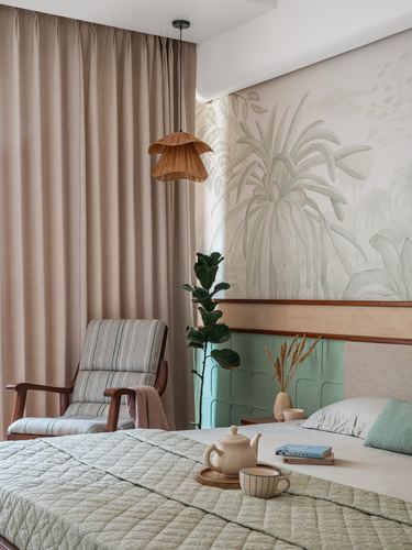 Bedroom corner with cane pendant, striped armchair, botanical mural, and quilted bed tray setting