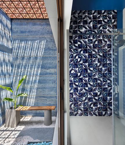 Outdoor courtyard with concrete bench and plant beside a patterned blue mosaic tiled bathroom shower.