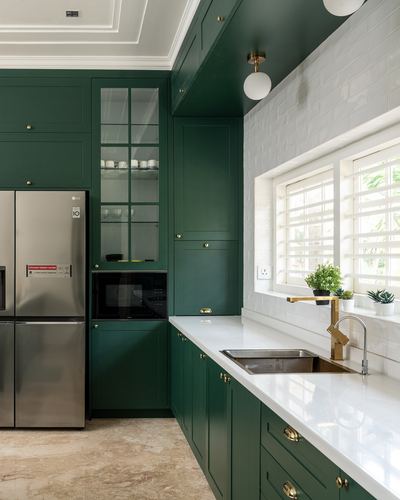 Green shaker kitchen with white brick backsplash, brass fixtures, and stainless steel fridge