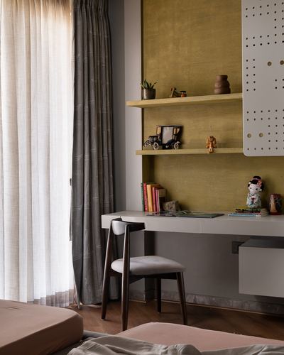 Study nook with mustard textured wall, floating wood shelves, desk and chair by sheer curtain