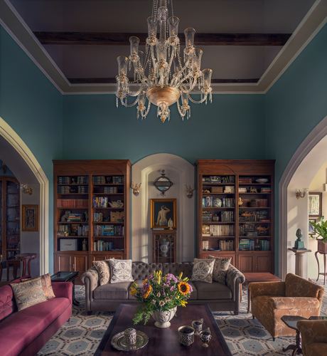 Grand teal living room with crystal chandelier, symmetrical bookshelves, and chesterfield sofas under high ceilings