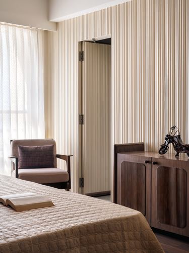 Bedroom corner with fluted paneled wall, mauve armchair, and ribbed wood cabinet