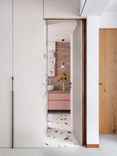View through a narrow doorway into a terrazzo-floored bathroom with pink vanity and sunflowers