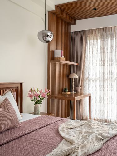 Bedroom corner with fluted wood panelling, mushroom pendant light, small wood console, and pink bedding