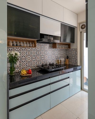 Galley kitchen with pale blue cabinetry, black countertop, and patterned tile backsplash