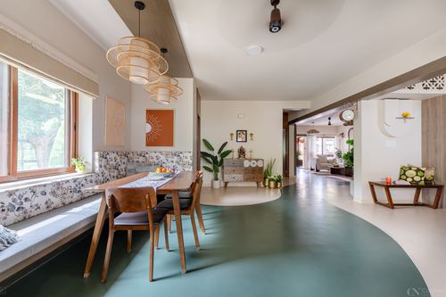 Open dining area with floral banquette, wooden table, layered pendant lights, and curved green terrazzo floor