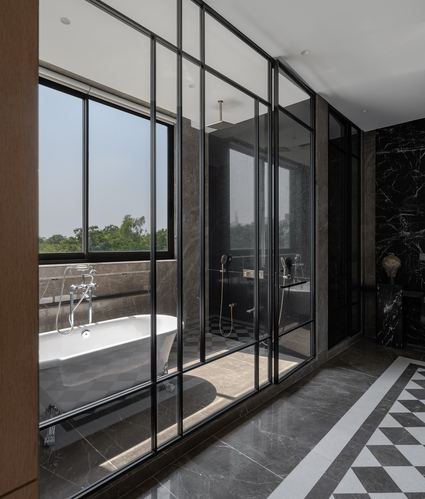 Bathroom with freestanding tub behind black-framed glass, marble floor, and window view of trees