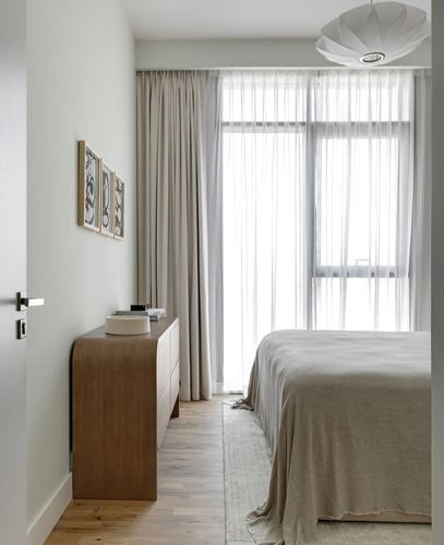 Minimalist bedroom with curved wood dresser, sheer curtains, and sculptural pendant light