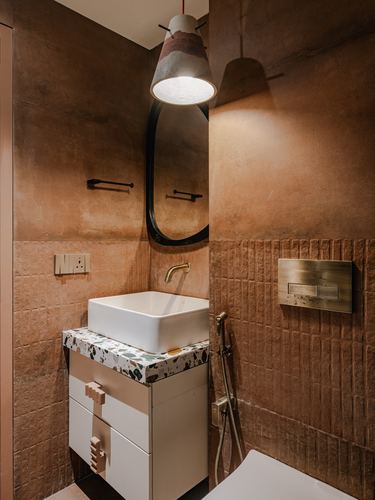 Small terracotta-toned bathroom with vessel sink, oval mirror and terrazzo counter