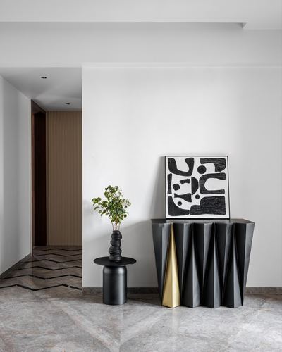 Black faceted console with abstract art and plant in a white marble-floored foyer