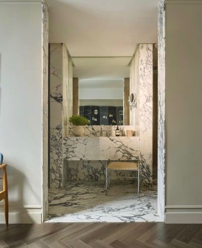 Marble-clad bathroom vanity seen through a doorway, herringbone wood floor in foreground