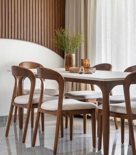 Wooden dining table with marble top surrounded by curved-back wood chairs against fluted wood wall