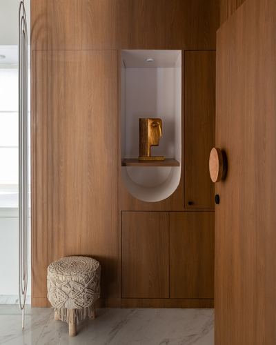 Wood-paneled foyer wall with arched niche holding a brass sculpture and macrame stool below